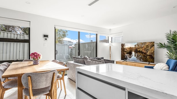 A modern kitchen with a large island, dining area with chairs, and a TV on the wall.