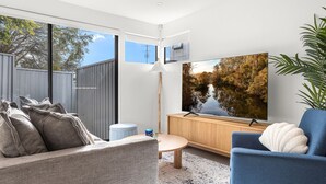 A modern living room with a large window, a sofa, a blue armchair, a wooden cabinet, and a large painting of a waterfall.