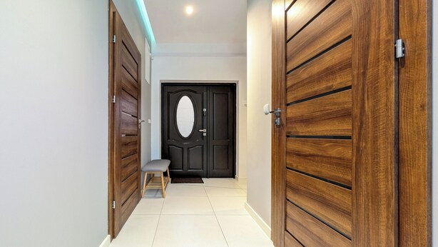Un couloir avec des portes en bois, un banc et une porte noire dotée d’une fenêtre ronde.