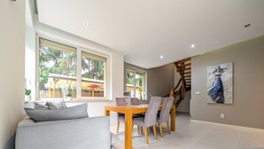 Un salon moderne avec un canapé, une table à manger et des chaises. Un escalier mène à un autre niveau.