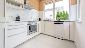 Une cuisine moderne avec des armoires blanches, une hotte de cuisinière en acier inoxydable, un lave-vaisselle et une fenêtre donnant sur les arbres.