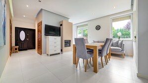 Un salon moderne comprenant un coin repas, un téléviseur fixé sur un meuble et une grande fenêtre laissant entrer la lumière naturelle.