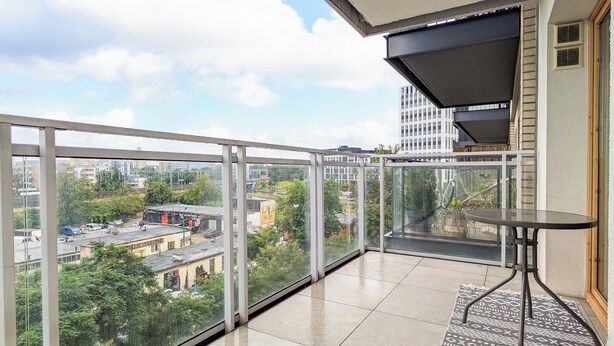 A balcony with a glass railing, a small table, and a patterned rug. - Riverwalk Charming Apartment (Wrocław)