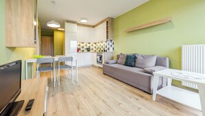 A modern kitchen with white cabinets, a dining area with a table and chairs, a sofa, and a TV. - Riverwalk Charming Apartment (Wrocław)