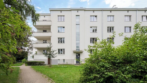 A multi-story residential building with a paved pathway leading to the entrance.