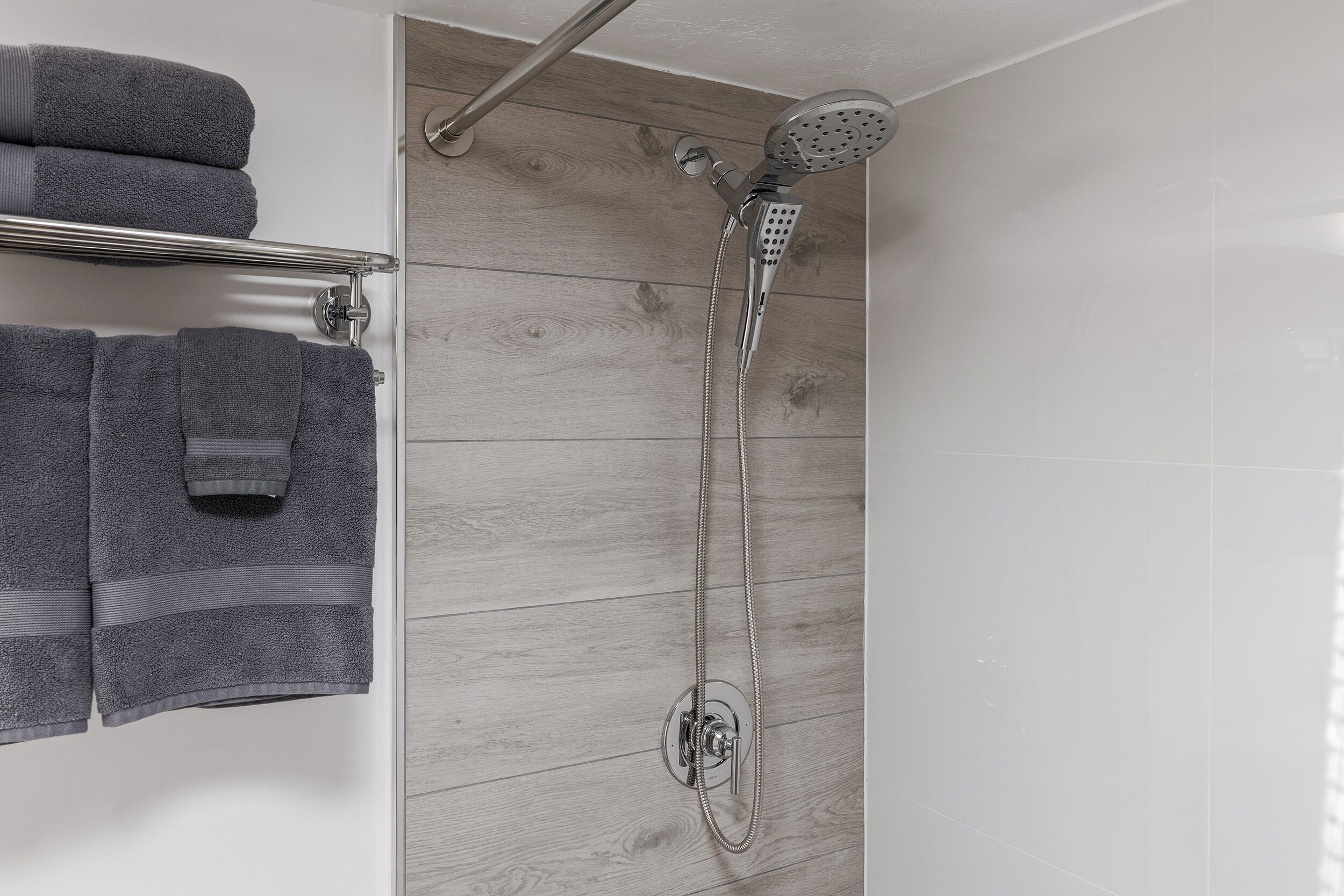 A shower with a handheld showerhead and a wall-mounted control panel.