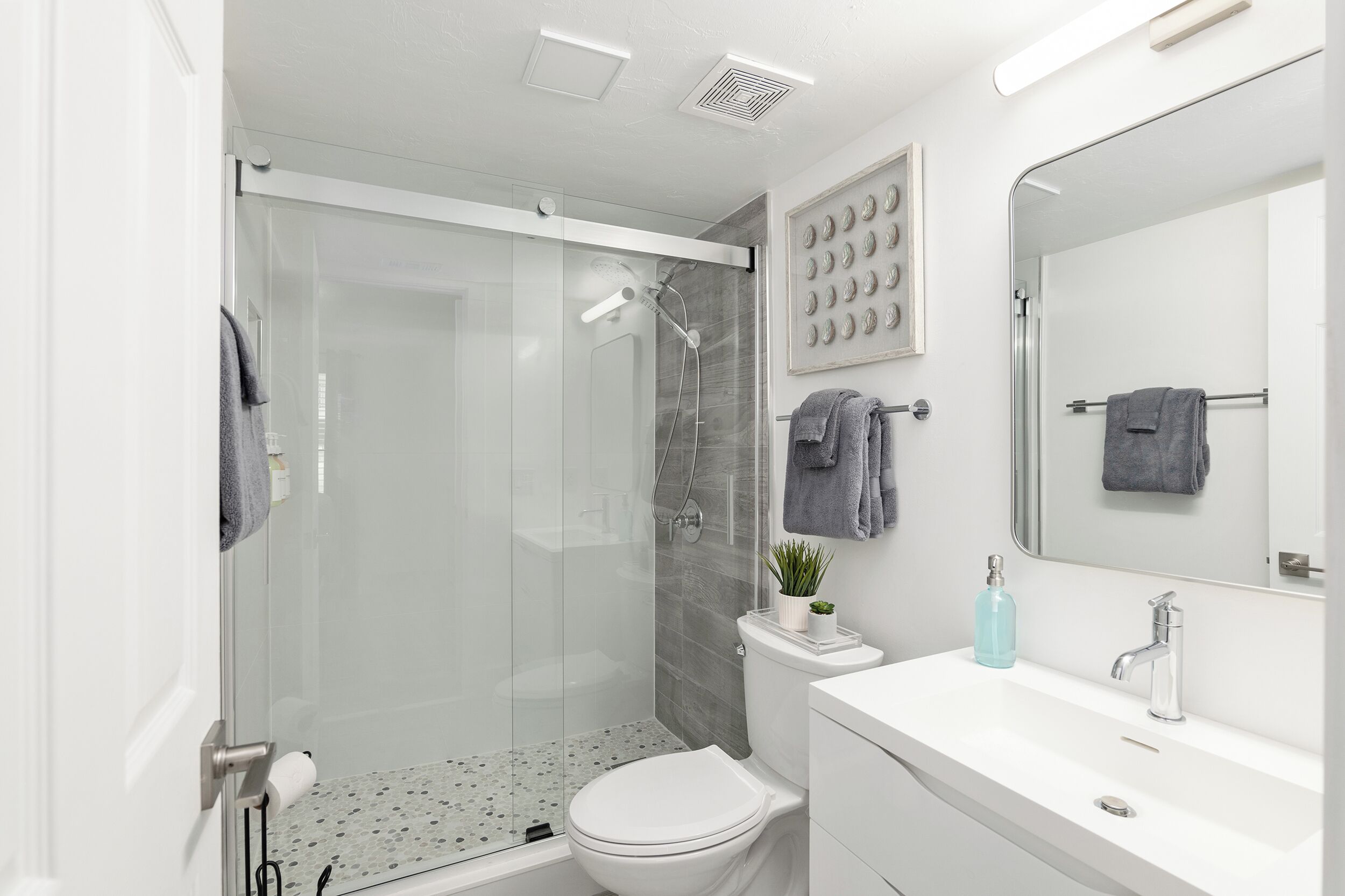 Un baño moderno con cabina de ducha de vidrio, inodoro, lavamanos con espejo y barra para toallas.