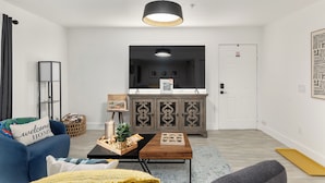 Ein modernes Wohnzimmer mit einem blauen Sofa, einem Holztisch und einem grauen Sessel. Es gibt eine Kommode mit dekorativen Türen und eine Hängelampe.