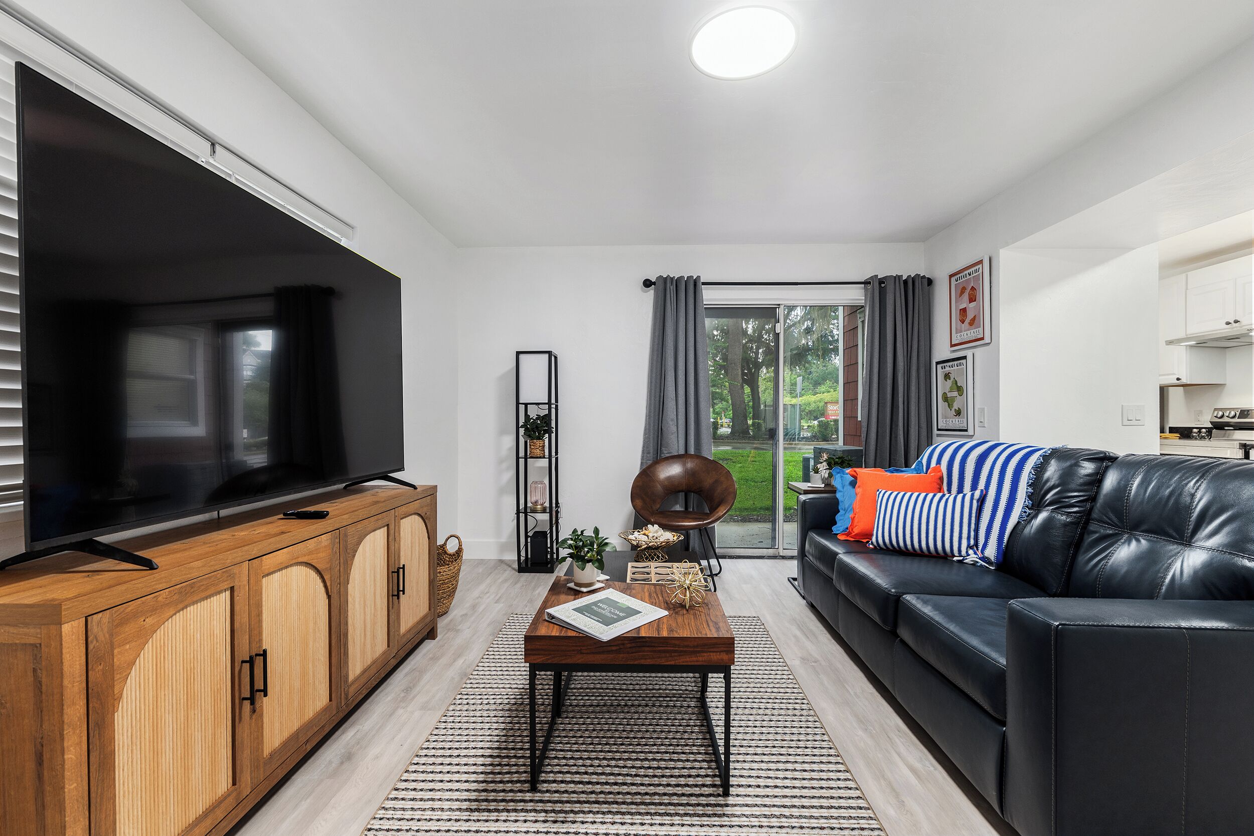 Una sala moderna con televisor, aparador de madera, sofá de cuero negro y una zona de comedor con mesa y sillas.