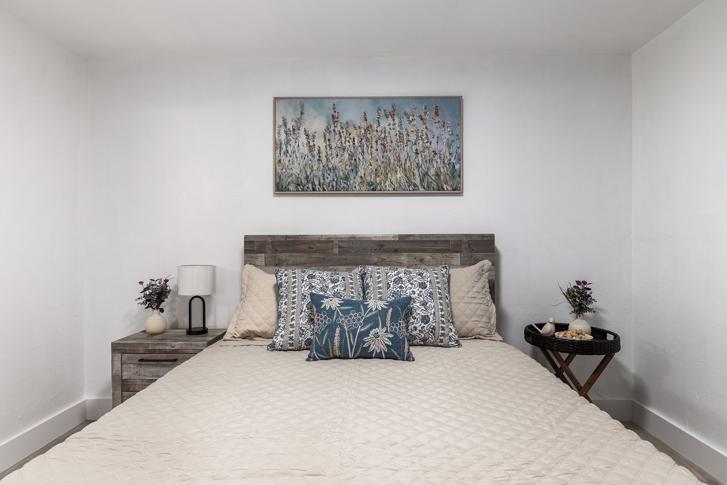 A bedroom with a bed, a nightstand, a lamp, and a wall-mounted painting.