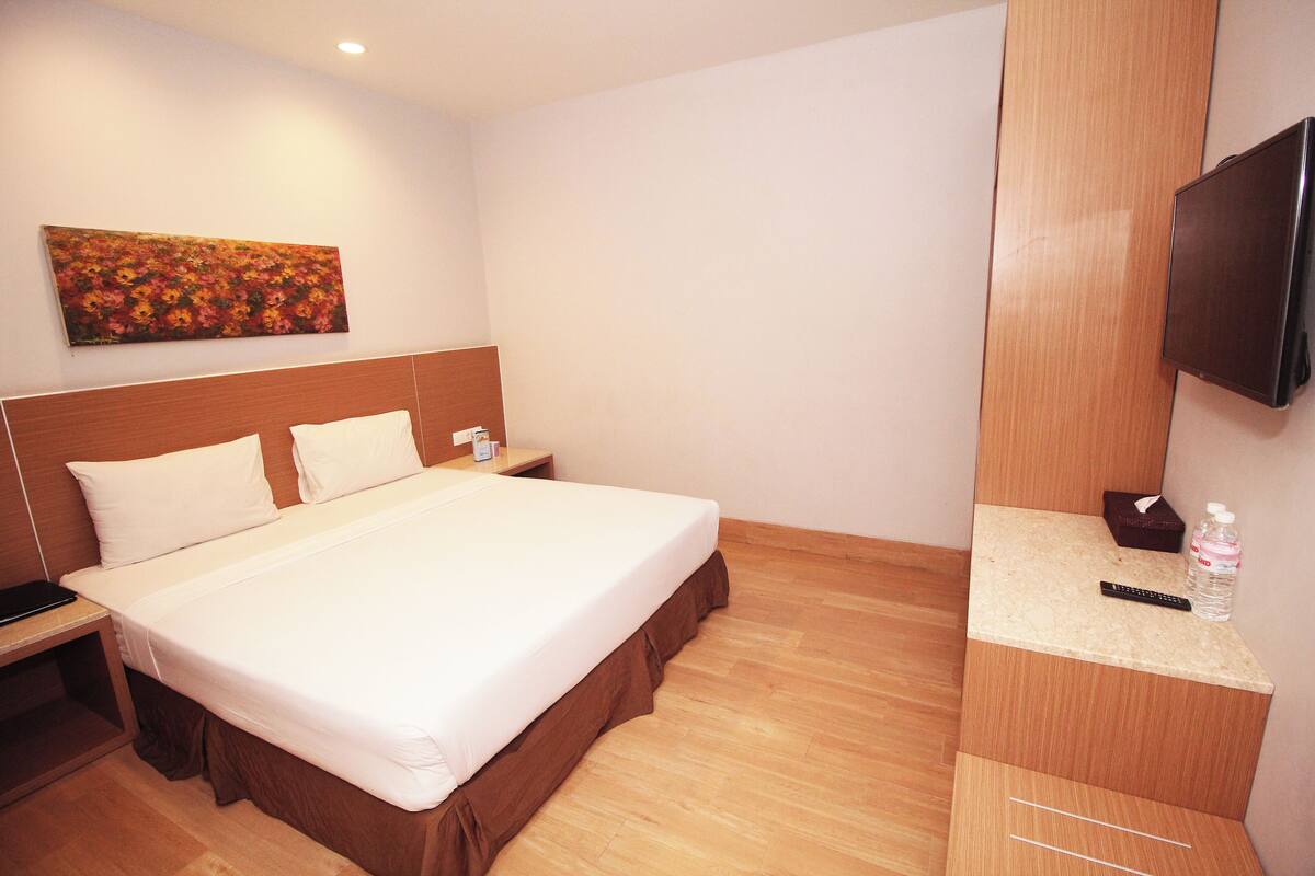 Een hotelkamer met een groot bed, een houten hoofdbord, een flatscreen televisie aan de muur en een schilderij boven het bed.