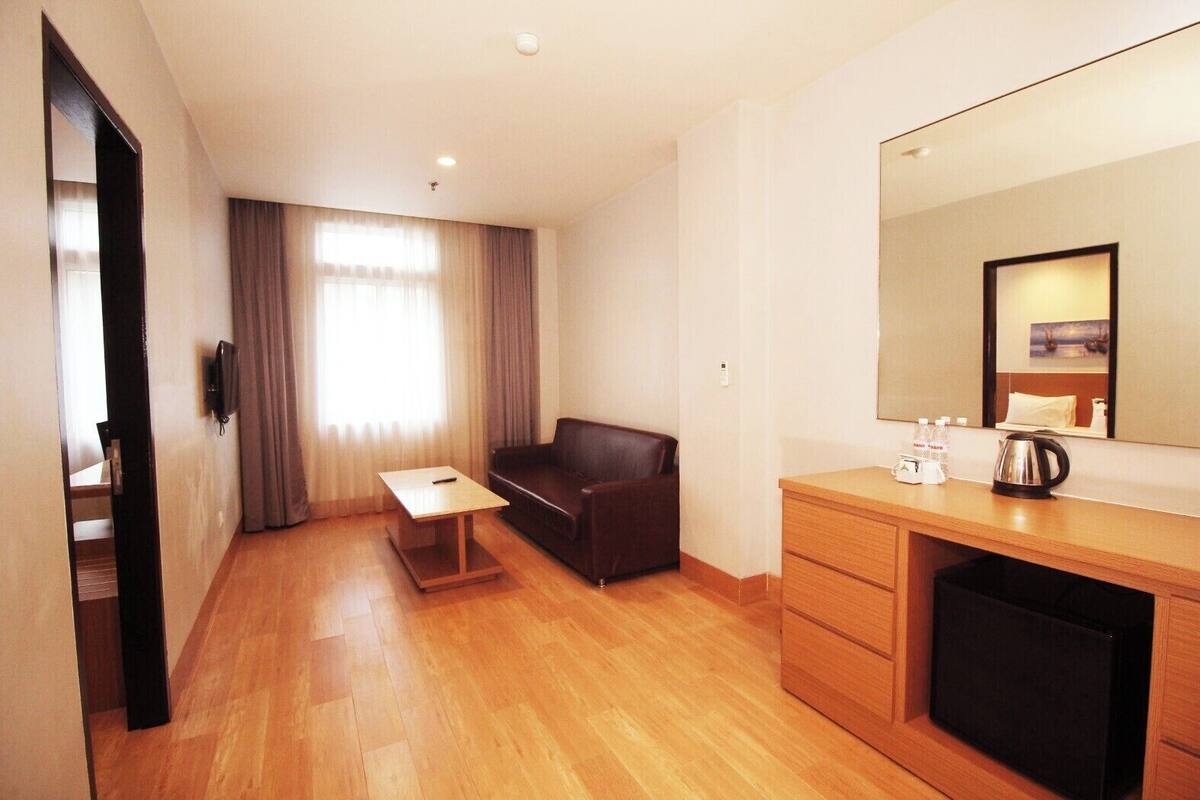 Hotelkamer met houten vloer, een bank, een klein tafeltje, een bureau, een spiegel en een minibar.