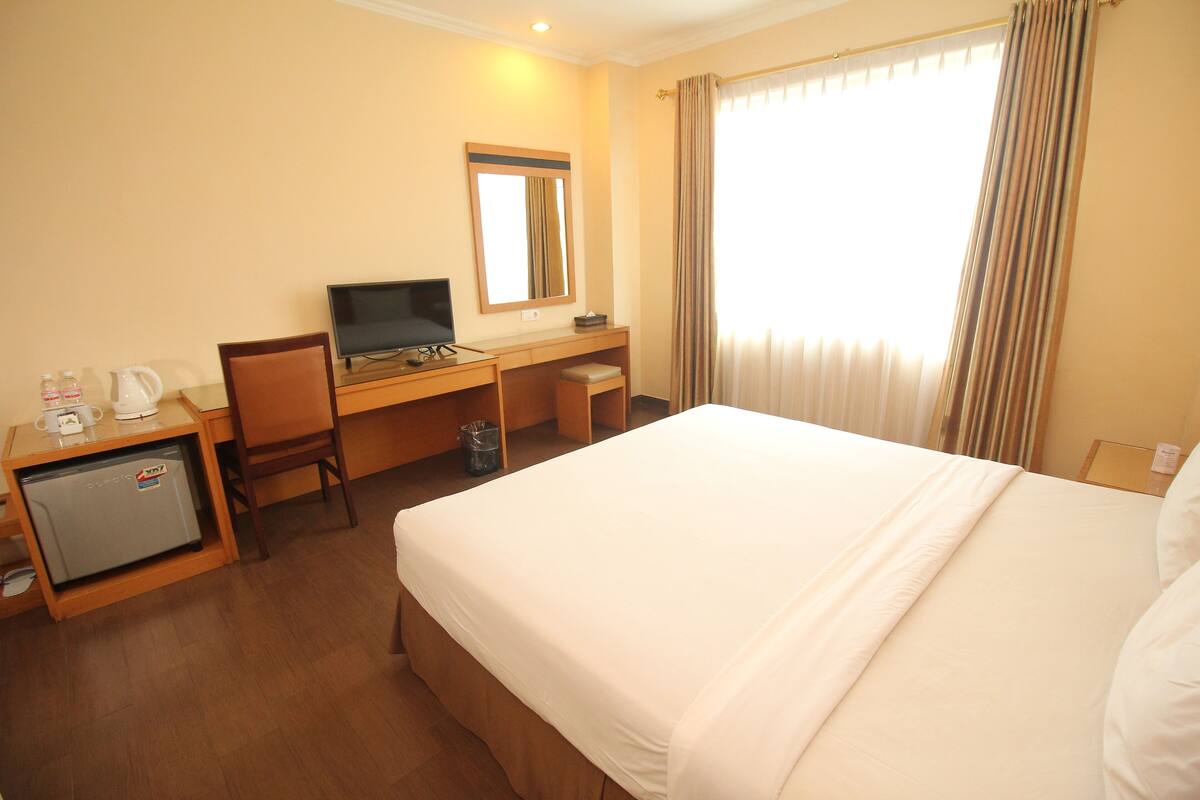 Een hotelkamer met een bed, bureau, stoel en een kleine koelkast.