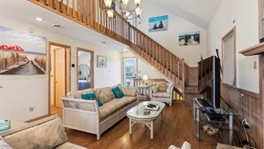 Un salon spacieux avec un escalier en bois, une grande télévision et un coin salon confortable.