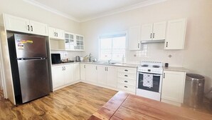 A modern kitchen with white cabinets, a stainless steel refrigerator, a stove, and a wooden dining table. - 3BDR Blue Mountains Hideaway in Central Katoomba (Katoomba)