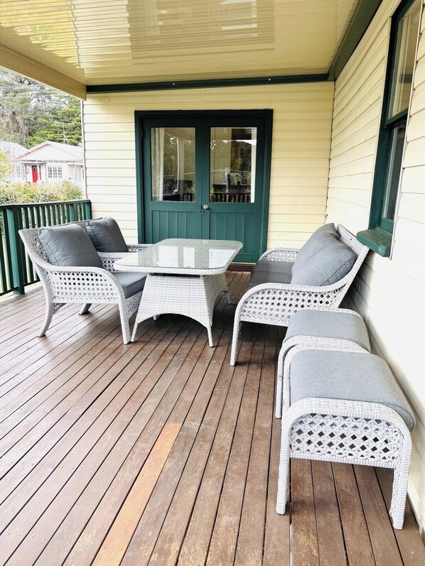 A covered porch with a table and four wicker chairs.