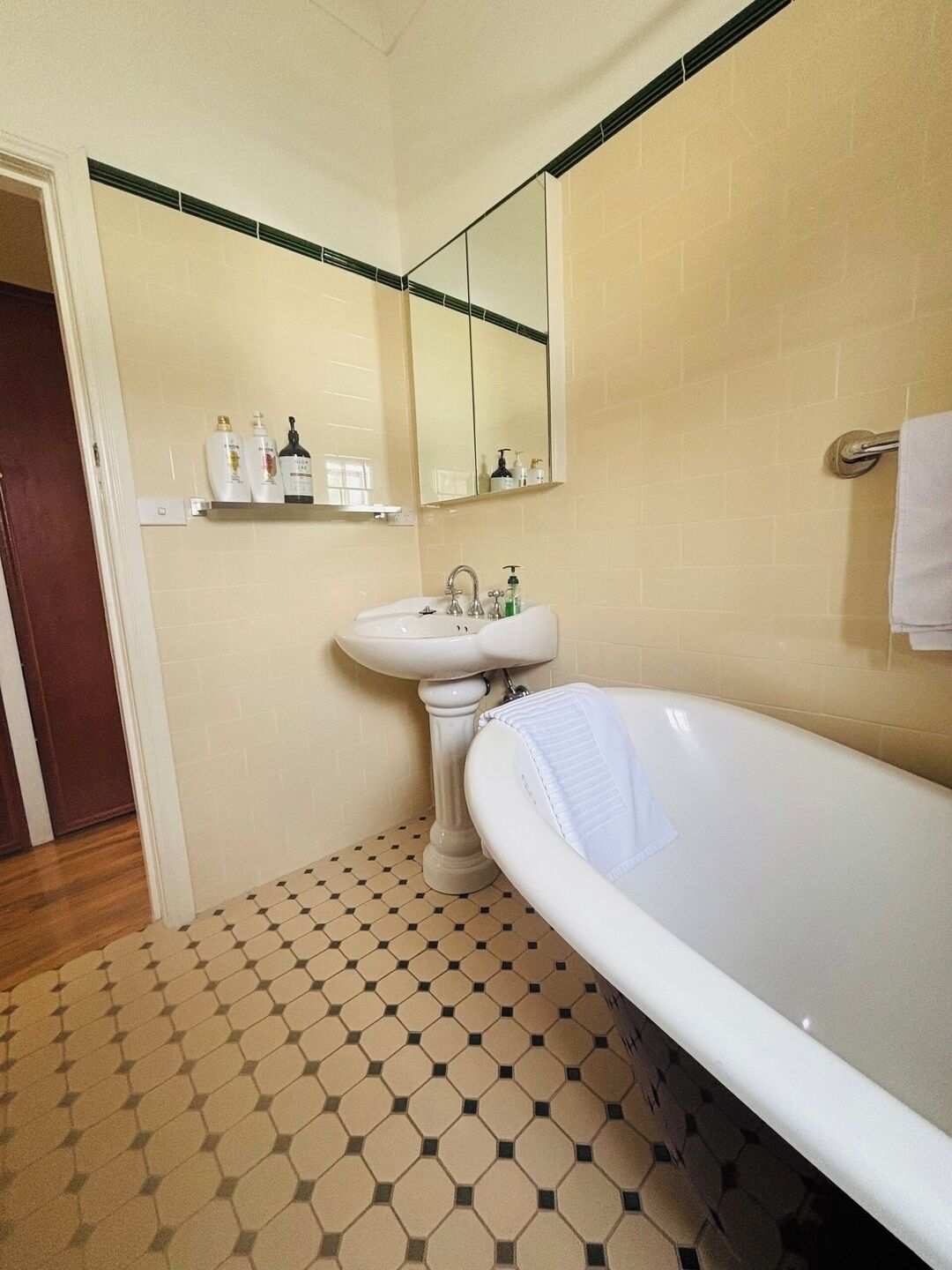 A bathroom with a white bathtub, a sink, and a mirror. There is a shelf with toiletries above the sink.