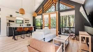 A modern kitchen with a central island, a dining area with a white sofa and chairs, and large windows offering a view of the outdoors. - Relaxing Ranch, Friendly Animals, Modern Stay (Cedar Creek)
