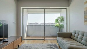 Una sala moderna con puerta de cristal corredera que da a un balcón, televisor de pantalla plana, sofá y una planta pequeña.