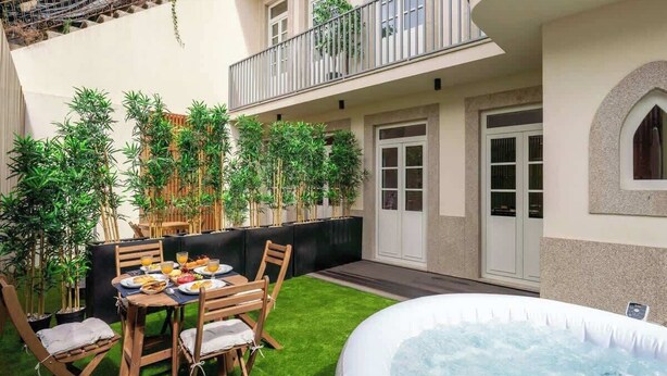 A patio with a dining table, chairs, and a hot tub. There are potted plants and a balcony with a railing. - Terrace & Jacuzzi in Heart of Porto by HostWise (Porto)