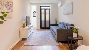 A modern living room with a grey sofa, a small side table with a plant, a white cabinet, and a TV on a stand. - Terrace & Jacuzzi in Heart of Porto by HostWise (Porto)