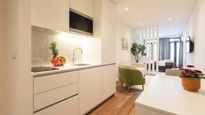 A modern kitchen with white cabinets, a stainless steel sink, and a built-in microwave. There is a dining area with a white table and a green chair. - Terrace & Jacuzzi in Heart of Porto by HostWise (Porto)