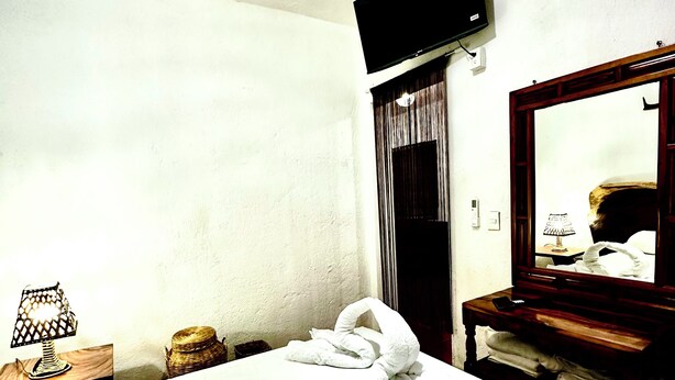A hotel room with a bed, a TV mounted on the wall, a wooden nightstand, and a mirror. - Ocean Colors Villa (San Pedro Pochutla)