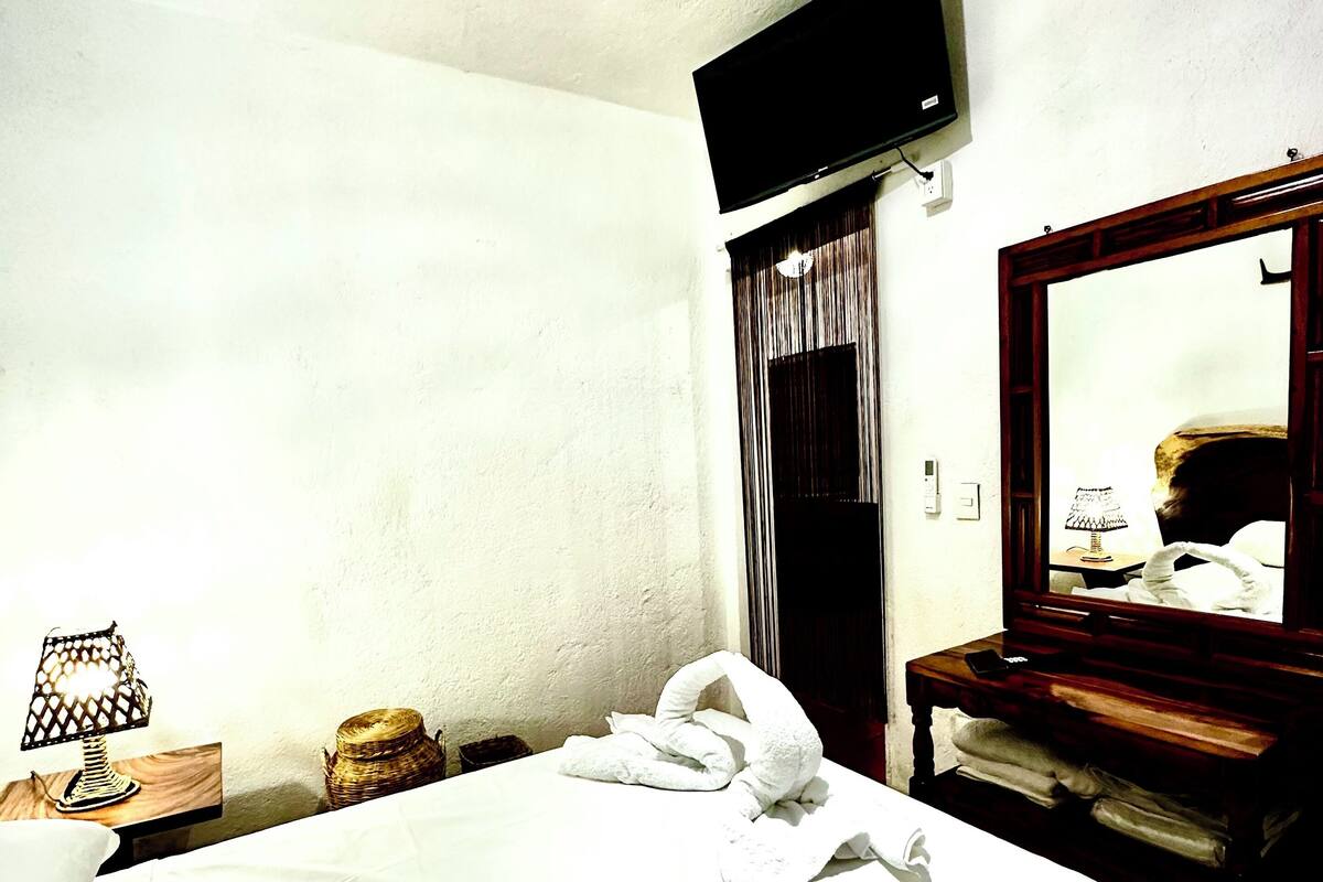 A hotel room with a bed, a TV mounted on the wall, a wooden nightstand, and a mirror.