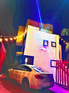 A white car parked in front of a building with a red gate and string lights. - Ocean Colors Villa (San Pedro Pochutla)