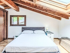 Una camera da letto con un letto, travi in legno a soffitto, una finestra con vista e un comodino con una lampada.
