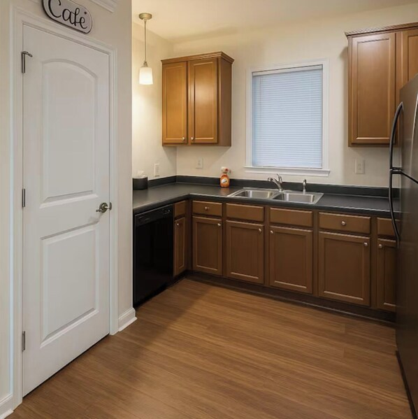 A kitchen with wooden cabinets, a black countertop, a sink, and a window with blinds.