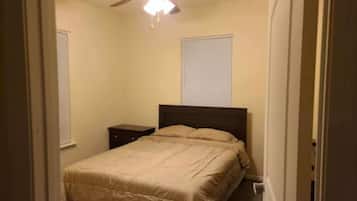 Een slaapkamer met een bed, nachtkastje, plafondventilator en een raam met jaloezieën.