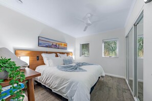 A bedroom with a bed, a ceiling fan, a painting, and a window.