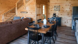 A wooden interior with a dining table set for four, a sofa, and a staircase. - Cabin w/ River Boat Ramp~Private HotTub~Sauna~Lake Cumberland~Firepit~Pickleball (Jamestown)