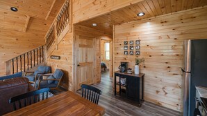 A wooden cabin interior with a dining area, a staircase, and a kitchen. - Cabin w/ River Boat Ramp~Private HotTub~Sauna~Lake Cumberland~Firepit~Pickleball (Jamestown)