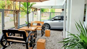 Un espacio al aire libre cubierto con mesas y bancos, un coche estacionado cerca y vistas del entorno verde.