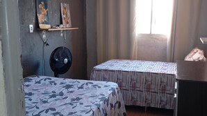 A small, compact room with two single beds, a fan, and a small table. - Casa do Betto  (Aracaju)