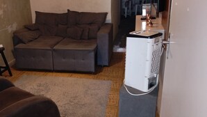 A living room with a sofa, a small table, a fan, and a refrigerator. - Casa do Betto  (Aracaju)