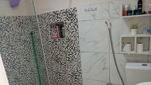 A bathroom with a shower, toilet, and a shelf with toiletries. - Casa do Betto  (Aracaju)
