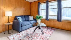 A cozy room with a blue sofa, a small table with a vase of flowers, and a window with curtains. - Huckleberry Lodge Mountain Getaway Near Banff! (Harvie Heights)