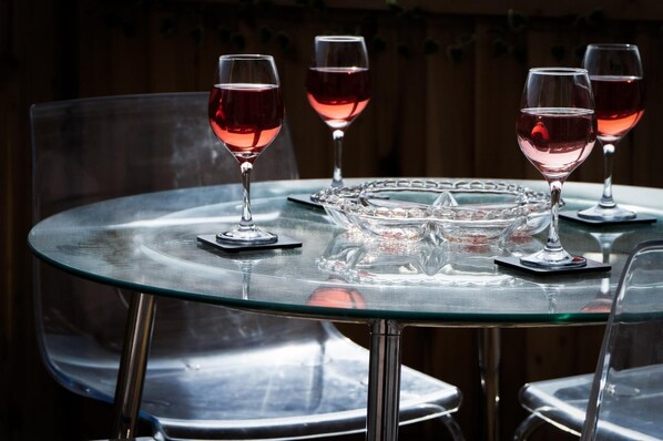 Una mesa redonda de vidrio con cuatro copas de vino llenas de vino tinto, un cuenco de vidrio transparente y posavasos de metal.