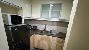 A compact kitchen with a refrigerator, microwave, sink, and a small window above the counter. - Chic 1-bedroom building in fantastic Pasay City with AC, fitness room (Pasay City)