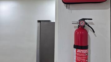 Un extintor rojo sujeto a la pared, con instrucciones y un botiquín de primeros auxilios cerca.