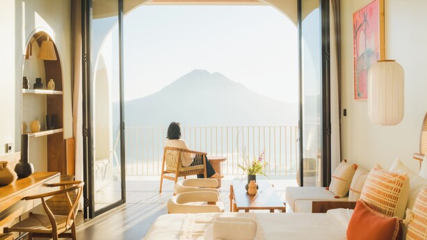 Una habitación con cama, una silla, una mesa y vista a la montaña a través de una puerta de vidrio.