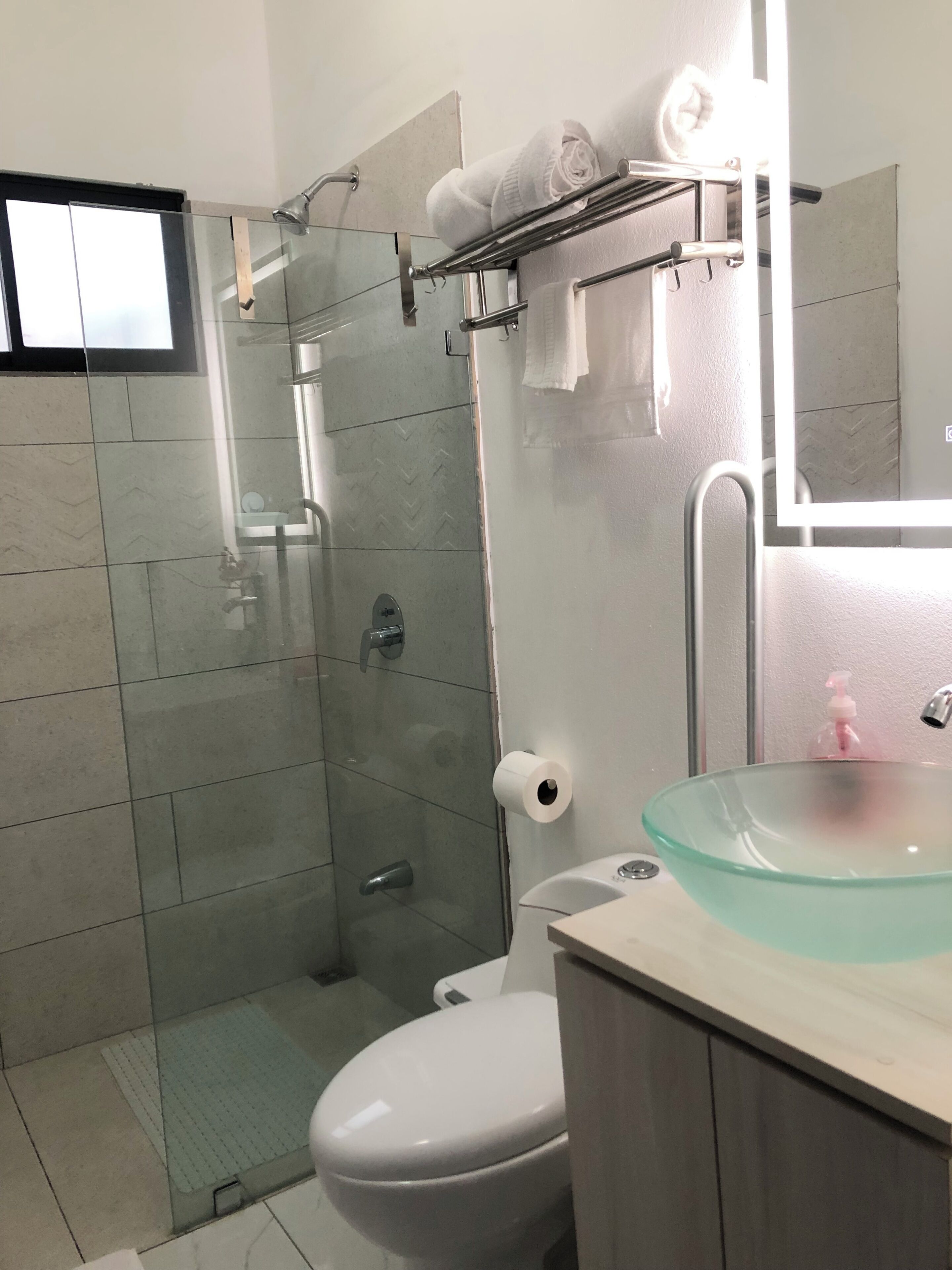 A modern bathroom with a glass shower enclosure, a white toilet, and a glass sink with a soap dispenser.