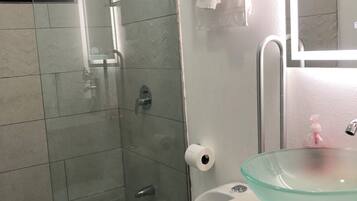 A modern bathroom with a glass shower enclosure, a white toilet, and a glass sink with a soap dispenser.