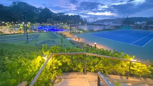 A tennis court with surrounding greenery and a pathway. - Family condo with resort-style pools, close to beaches, nature and adventure. (puntarenas)
