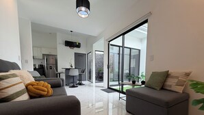 A modern living room with a sofa, a dining area with a table and chairs, a kitchen, and a sliding glass door leading to an outdoor area. - Family condo with resort-style pools, close to beaches, nature and adventure. (puntarenas)