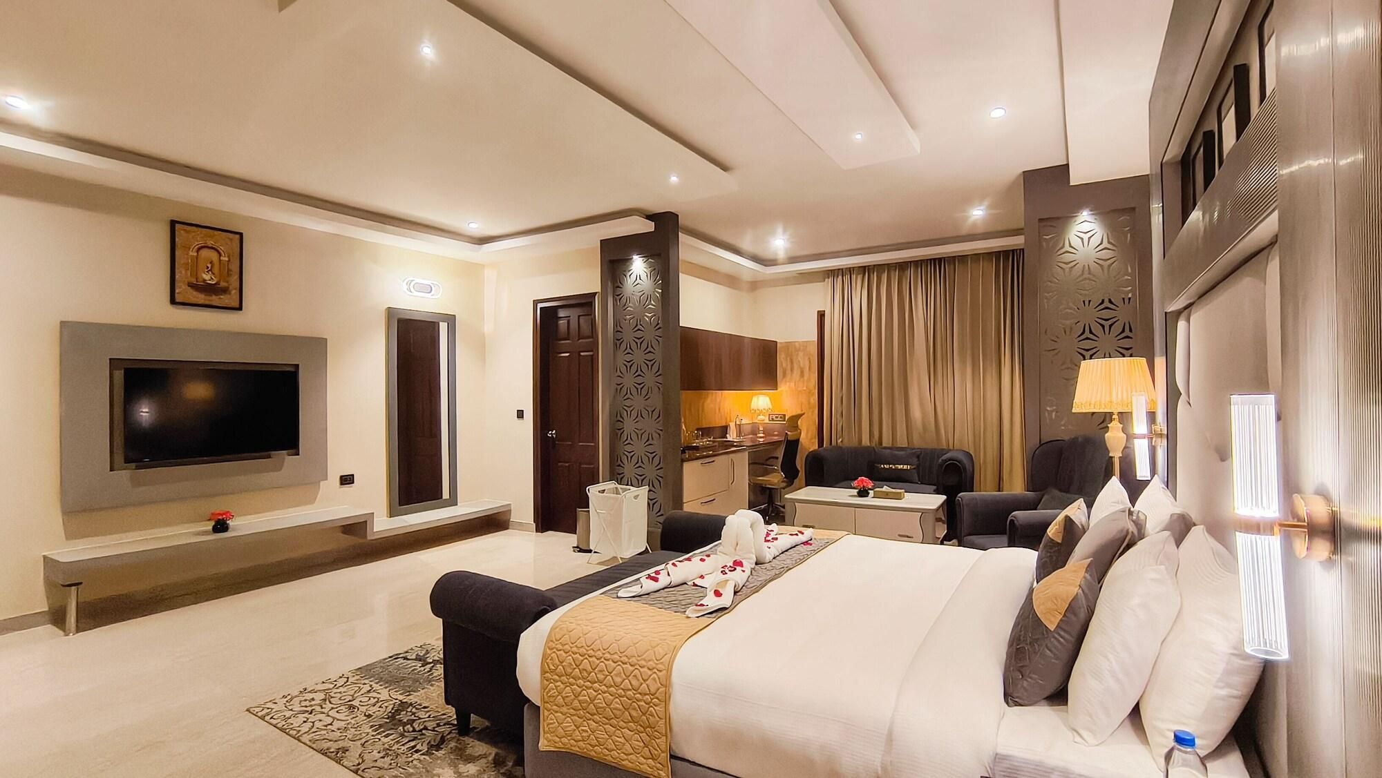 A modern hotel room with a large bed, a flat-screen TV, a desk, and a seating area.