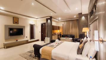 A modern hotel room with a large bed, a flat-screen TV, a desk, and a seating area.